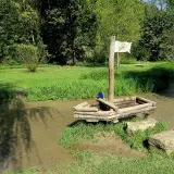 Ein hölzernes Piratenschiff mit einem Kind an Bord im Wolfstal Lauterach. Ein weiteres Kind spielt im Wasser.