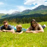 Familie genießt die Aussicht auf die Berge in der Schweiz, liegend auf einer grünen Wiese.