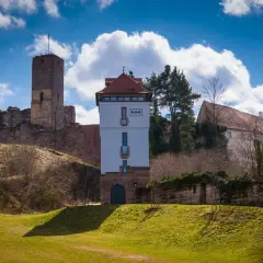 Die Ruine Wartstein mit einem modernen Turm und alten Gemäuern unter blauem Himmel mit Wolken.