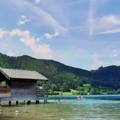 Holzhütte am See, Menschen planschen im Wasser. Perfekt für **Bayrischzell wandern mit Kindern** und Erfrischung.