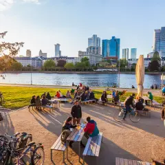 Frankfurt am Main: Menschen genießen das Leben am Mainufer mit Blick auf die Skyline. Hier kann man entspannen, Rad fahren und die Aussicht genießen.