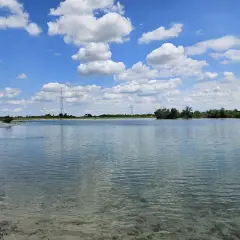Ein sonniger Tag am Hollerner See mit blauem Himmel, weißen Wolken und klarem Wasser.