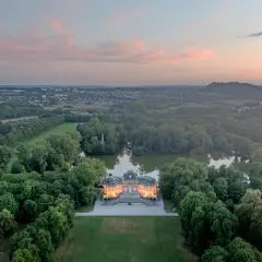 Schloss Monrepos Ludwigsburg, beleuchtet im Abendlicht, umgeben von einem See und üppigen Bäumen, mit Blick auf die Stadt.
