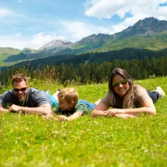 Familie genießt die Aussicht auf die Berge in der Schweiz, liegend auf einer grünen Wiese.