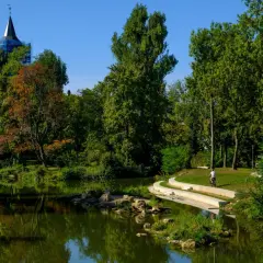 Ein Radfahrer fährt auf einem Weg am Wasser entlang, umgeben von Bäumen und einem Kirchturm.