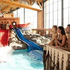Familie genießt die **Therme mit Kindern**. Ein Junge rutscht auf einer roten Wasserrutsche, während die Familie zusieht.