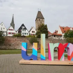 Bunte Buchstaben mit "#ulmdeinstadt" und "#ulmyourcity" vor historischer Kulisse. Hier kann man Ulm erleben!
