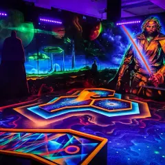 Galaktisches indoor schwarzlicht minigolf mit leuchtenden Bahnen und Weltraum-Kulisse. Ein Jedi mit rotem Lichtschwert wacht über das Spiel.