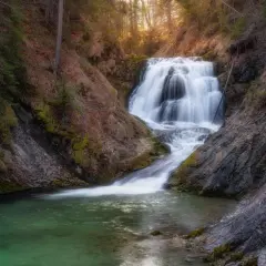 Ein malerischer Walchensee Wasserfall stürzt über Felsen in ein smaragdgrünes Becken. Umgeben von Bäumen und Moos, ein friedlicher Ort.