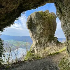 Blick durch eine Felsöffnung auf einen markanten Felsen mit Moosbewuchs. Ein Pfad führt entlang der Felsen. Eine tolle hohle Felsen Tour.