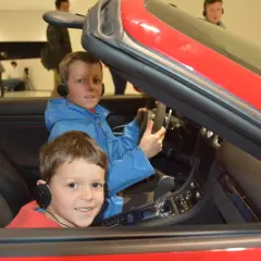 Zwei Jungen mit Kopfhörern sitzen in einem roten Porsche im Porsche Museum.