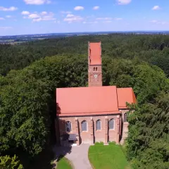 Kirche mit rotem Dach und Turm, umgeben von Wald. Ein historischer Ort, vielleicht einst Burg Wittelsbach.