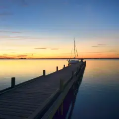 Holzsteg am Steinhuder Meer bei Sonnenuntergang, ein Segelboot liegt vertäut.