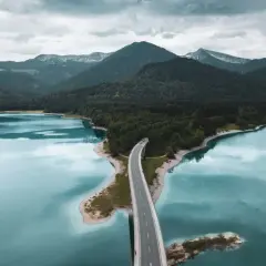 Brücke über türkisfarbenen See, umgeben von bewaldeten Bergen. Perfekt für einen Urlaub in Deutschland.