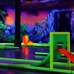 Ein Affe blickt auf leuchtende Bahnen beim Schwarzlicht Minigolf Heilbronn. Bunte Wandmalereien und Hindernisse schaffen eine Dschungel-Atmosphäre.