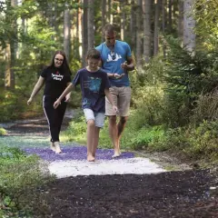 Familie genießt den Barfusspark Hallwangen. Barfuß über verschiedene Untergründe im Wald spazieren.