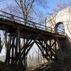 Holzbrücke führt zur Burgruine Rauber. Steinmauer mit Bogen und Schatten von Bäumen.