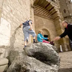 Ein Mann hilft Kindern beim Klettern auf einen Felsen vor einer Kirche in Trier.