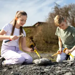 Zwei Kinder knien im Freien und graben mit Hämmern und Meißeln nach Fossilien. Vielleicht finden sie bald etwas Spannendes, wie bei Ausgrabungen in Stuttgart.