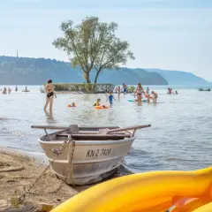 Menschen genießen das Bodensee Baden an einem sonnigen Tag. Kinder planschen im Wasser, während Boote am Ufer liegen.