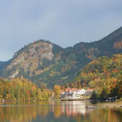 Zwei Märchenschlösser, Hohenschwangau und Neuschwanstein, thronen über einem See in Bayern, umgeben von bunten Herbstwäldern.