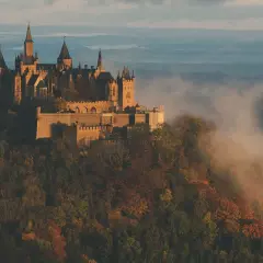 Burg Hohenzollern thront majestätisch auf einem Berg, umgeben von nebligen Herbstwäldern. Ein atemberaubender Aussichtspunkt.
