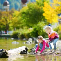 Zwei Mädchen genießen ihren Urlaub mit Kindern in Bayern am See. Sie spielen am Ufer im bunten Herbstlaub.