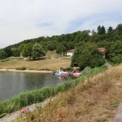 Sonniger Tag am badesee Zaberfeld. Menschen entspannen am Ufer, Kinder planschen im Wasser, Tretboote warten auf Ausflügler.