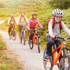 Fröhliche Familie auf einer Fahrradtour mit Kindern durch eine grüne Landschaft.