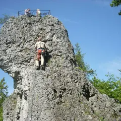 Kletterer erklimmt Felsen bei der Burgruine Wolfsberg. Oben genießen zwei Personen die Aussicht.