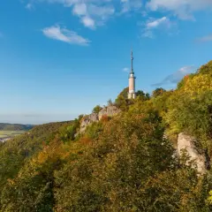 Der Schlossfelsenturm Albstadt ragt auf einem bewaldeten Felsen über der Stadt auf. Bunte Herbstfarben schmücken die Hänge.