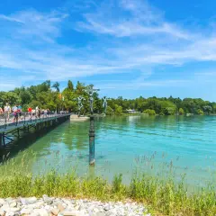 Menschen spazieren auf einer Brücke am Bodensee. Ein Denkmal mit Kreuzigungsgruppe steht im Wasser. Hier kann man in Konstanz viel unternehmen.