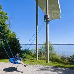 Ein Junge schaukelt am Starnberger See. Kinder genießen die Sonne und den Blick auf das Wasser.