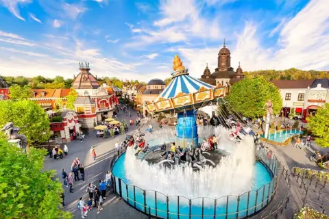 Ein bunter Kettenkarussell-Freizeitpark in Deutschland mit vielen Besuchern und einer beeindruckenden Fontäne.