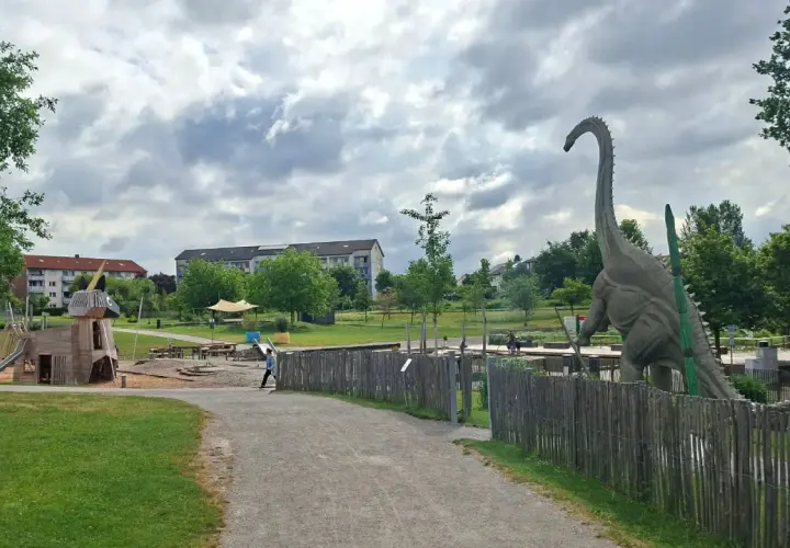 Ein riesiger Dinosaurier wacht über den Himmelsgarten mit Spielplatz.
