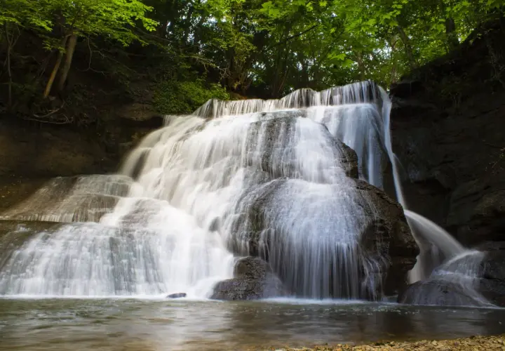 Ein üppiger, junger Wasserfall stürzt über moosbewachsene Felsen in ein ruhiges Becken.