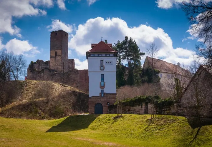 Die Ruine Wartstein mit einem modernen Turm und alten Gemäuern unter blauem Himmel mit Wolken.