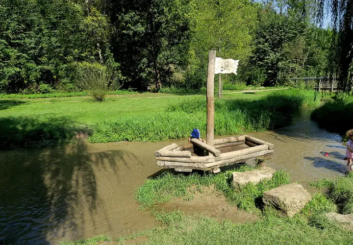 Ein hölzernes Piratenschiff mit einem Kind an Bord im Wolfstal Lauterach. Ein weiteres Kind spielt im Wasser.