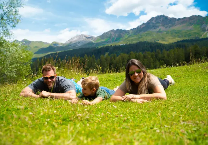 Familie genießt die Aussicht auf die Berge in der Schweiz, liegend auf einer grünen Wiese.