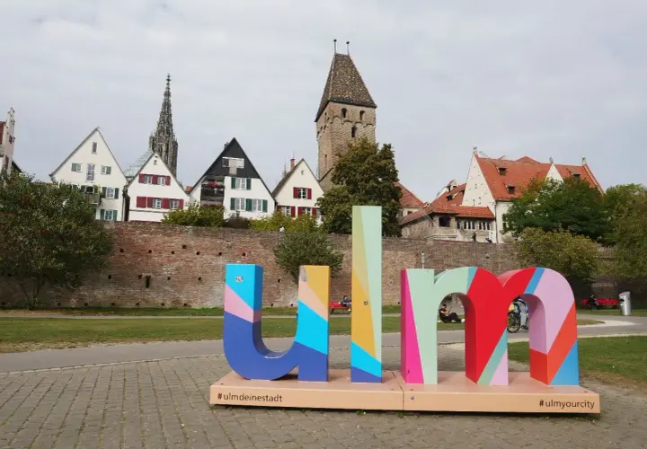 Bunte Buchstaben mit "#ulmdeinstadt" und "#ulmyourcity" vor historischer Kulisse. Hier kann man Ulm erleben!