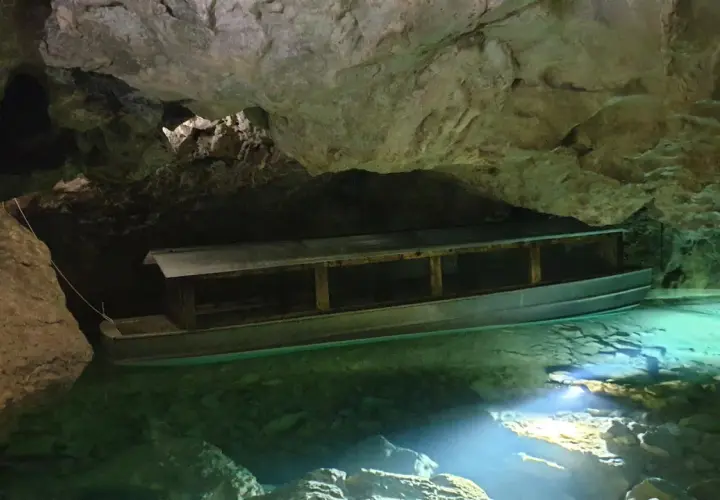 Ein Boot wartet auf Besucher in der Höhle der Zwiefalter Aach. Das klare, grüne Wasser schimmert im Licht.