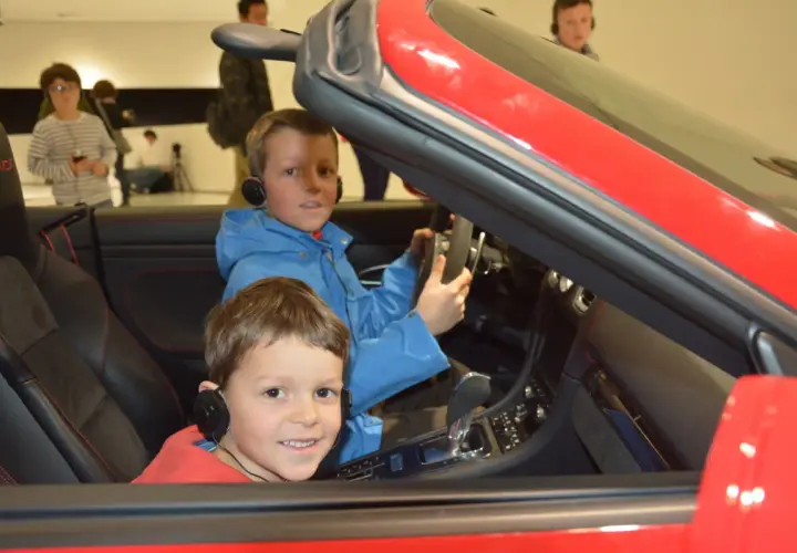 Zwei Jungen mit Kopfhörern sitzen in einem roten Porsche im Porsche Museum.