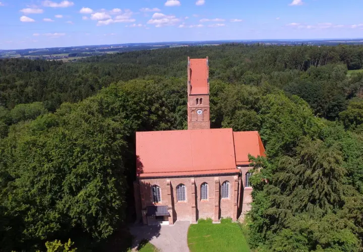 Kirche mit rotem Dach und Turm, umgeben von Wald. Ein historischer Ort, vielleicht einst Burg Wittelsbach.