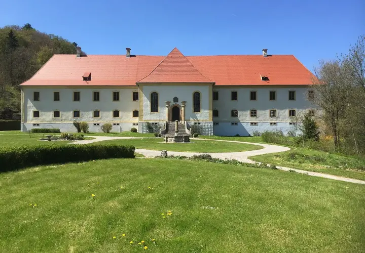 Schloss Ehrenfels bei Hayingen, ein imposantes Gebäude mit rotem Ziegeldach, umgeben von grünen Rasenflächen und Bäumen.
