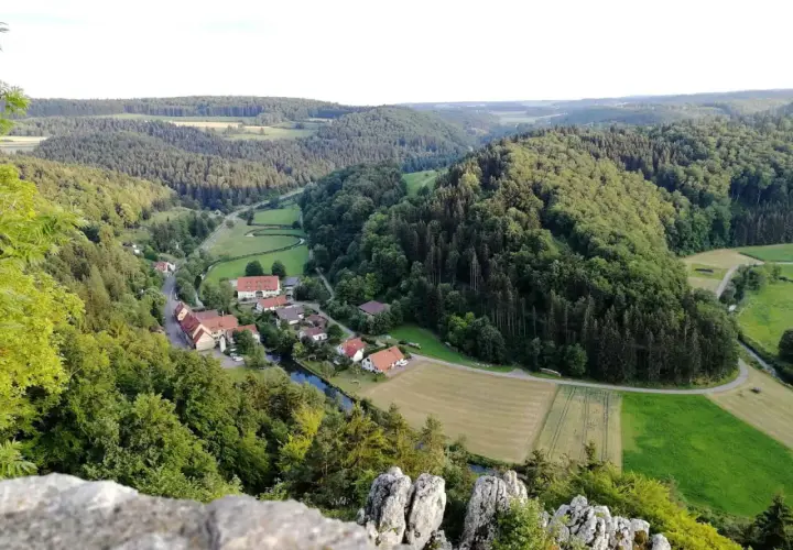 Idyllisches Lautertal Alb mit kleinen Dörfern, Flüssen und bewaldeten Hügeln, aufgenommen von einem Felsvorsprung.