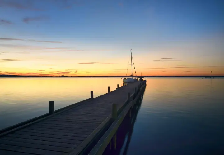 Holzsteg am Steinhuder Meer bei Sonnenuntergang, ein Segelboot liegt vertäut.