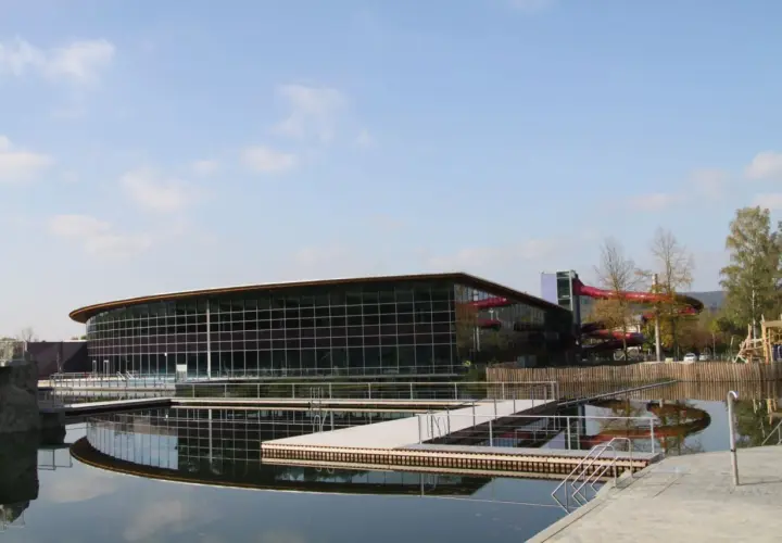 Moderner Badesee Schorndorf mit Glasfassade, Wasserrutschen und Stegen im Wasser.