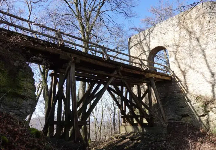 Holzbrücke führt zur Burgruine Rauber. Steinmauer mit Bogen und Schatten von Bäumen.