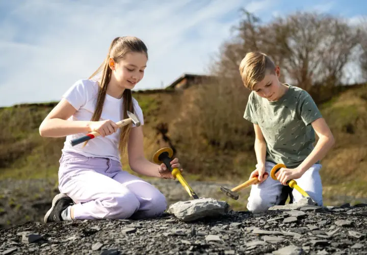 Zwei Kinder knien im Freien und graben mit Hämmern und Meißeln nach Fossilien. Vielleicht finden sie bald etwas Spannendes, wie bei Ausgrabungen in Stuttgart.