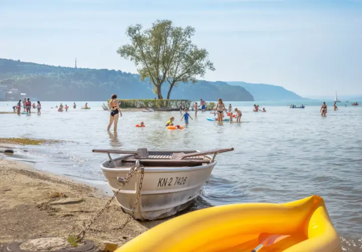 Menschen genießen das Bodensee Baden an einem sonnigen Tag. Kinder planschen im Wasser, während Boote am Ufer liegen.